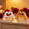 A pair of heart-shaped hand sculptures, one white and one gold, displayed on a surface with red roses.
