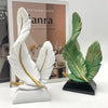 White and gold artistic feather sculpture centerpiece displayed in front of a book.