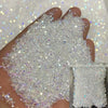 A hand is holding a pile of iridescent nail rhinestones for DIY art against a sparkling background.
