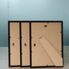Three black picture frames with light brown wood and acrylic fronts displayed on a wooden surface.