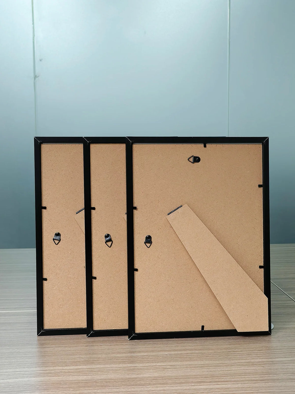 Three black picture frames with light brown wood and acrylic fronts displayed on a wooden surface.