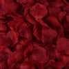Gros plan de pétales de roses artificielles rouge foncé éparpillés sur une surface.