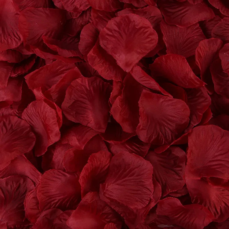 Gros plan de pétales de roses artificielles rouge foncé éparpillés sur une surface.