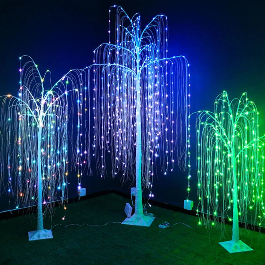 A large weeping willow tree illuminated with vertical strands of blue and green LED lights in a dark setting.