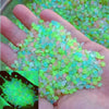 A hand holds a pile of glow-in-the-dark luminous green and pink pebbles.