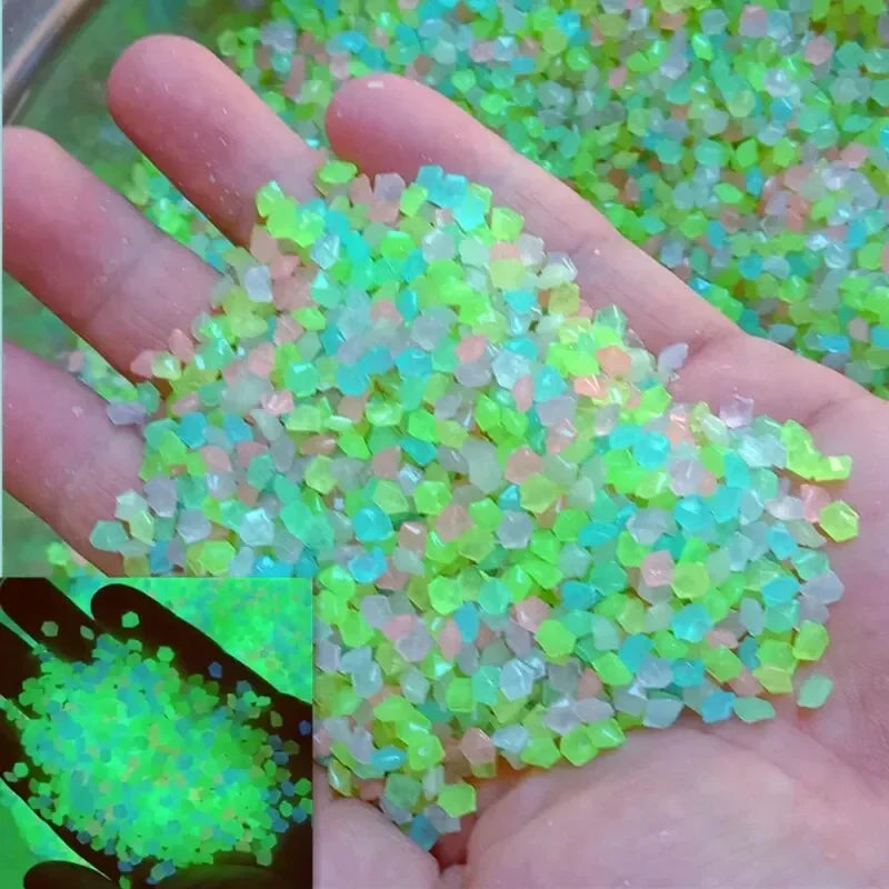 A hand holds a pile of glow-in-the-dark luminous green and pink pebbles.