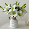 A bouquet of white artificial lilies with green buds in a white textured vase.