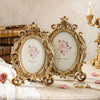 Vintage gold oval resin picture frame displayed on a marble surface with roses and a quill pen.