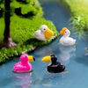 Petites sculptures d'animaux en résine de canards et d'un flamant rose flottant dans l'eau claire parmi le feuillage vert.