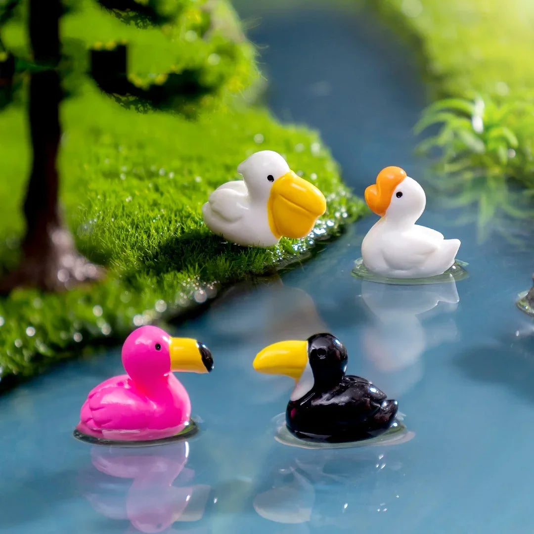 Petites sculptures d'animaux en résine de canards et d'un flamant rose flottant dans l'eau claire parmi le feuillage vert.