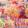 A close-up of a large quantity of colorful lollipops packaged in clear plastic with paper sticks and tie closures.