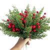 A hand holds a bouquet of artificial Christmas berry stems with pine branches featuring bright red berries.