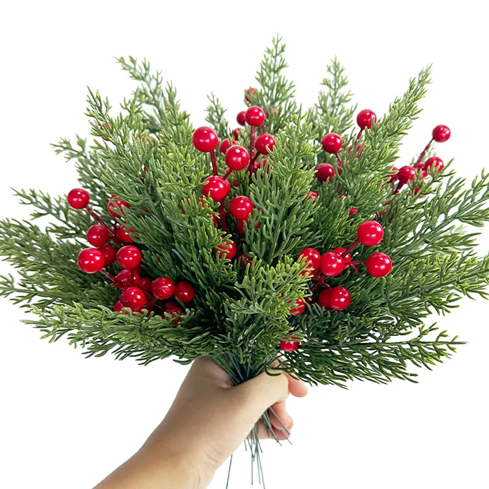 A hand holds a bouquet of artificial Christmas berry stems with pine branches featuring bright red berries.