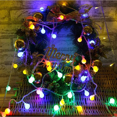 A festive wreath made of dark greenery and illuminated with purple and yellow string lights.