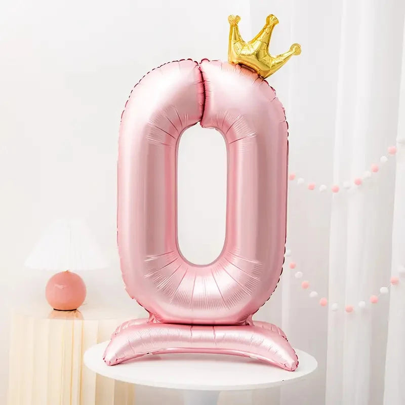 A pink foil number balloon shaped like the number 0 with a gold crown on top and a matching stand.