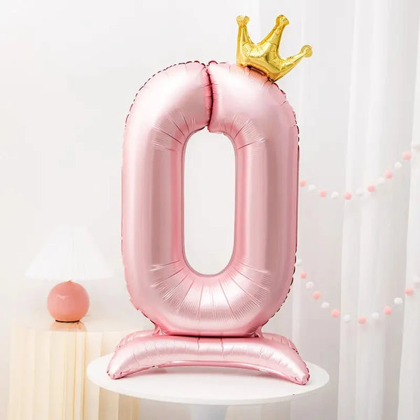 A pink foil number balloon shaped like the number 0 with a gold crown on top and a matching stand.