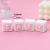 Four white baby blocks with pink letters B A B Y arranged in a row on a pink background