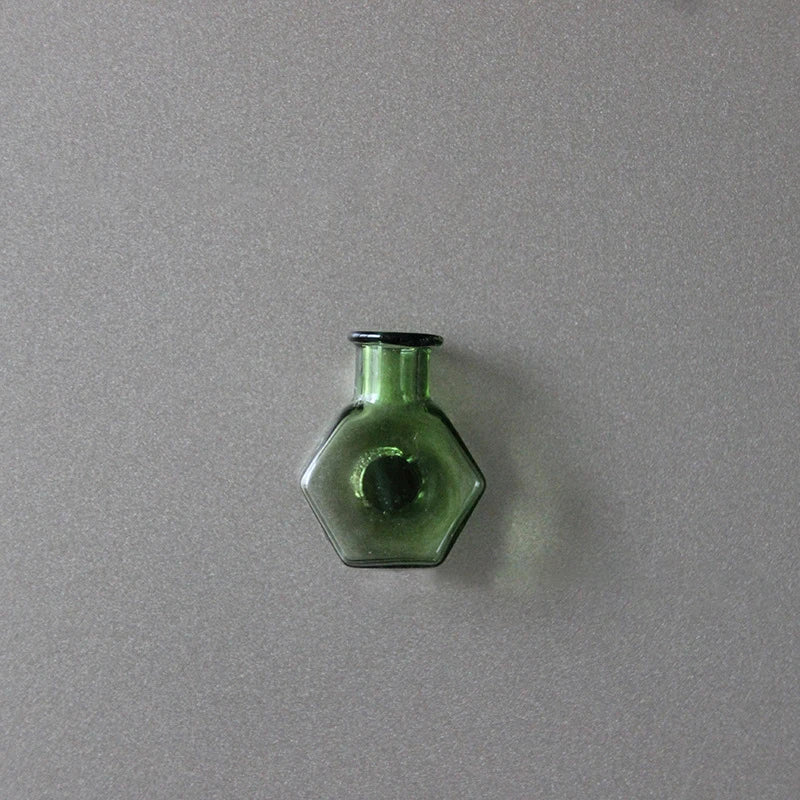 A small, green glass bottle-shaped fridge magnet against a gray background.