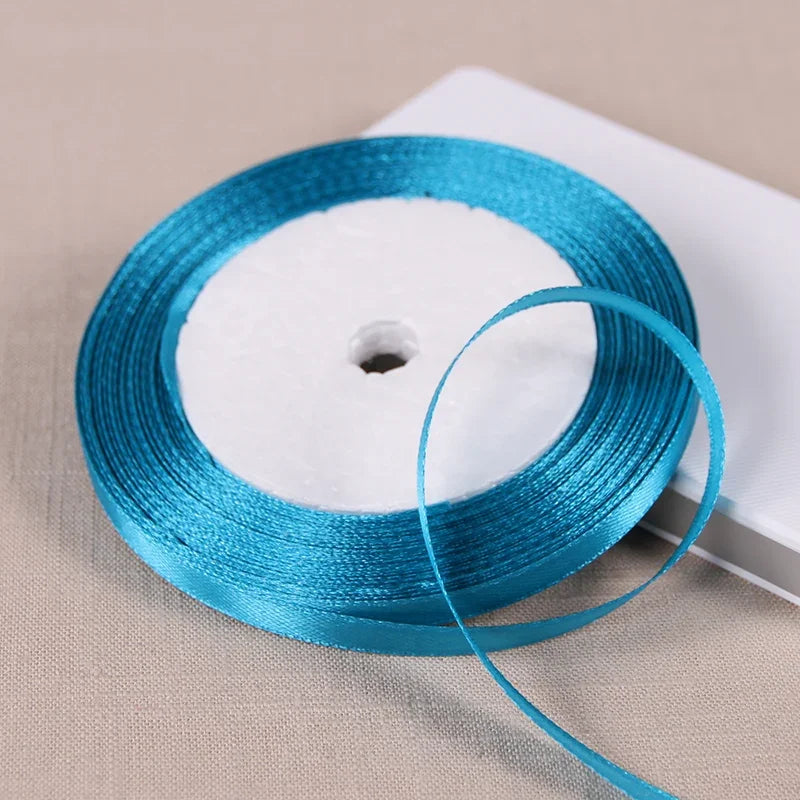 A spool of bright blue satin ribbon is shown on a white surface.