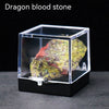 A rough, reddish-green dragon blood stone crystal specimen displayed inside a clear glass box.