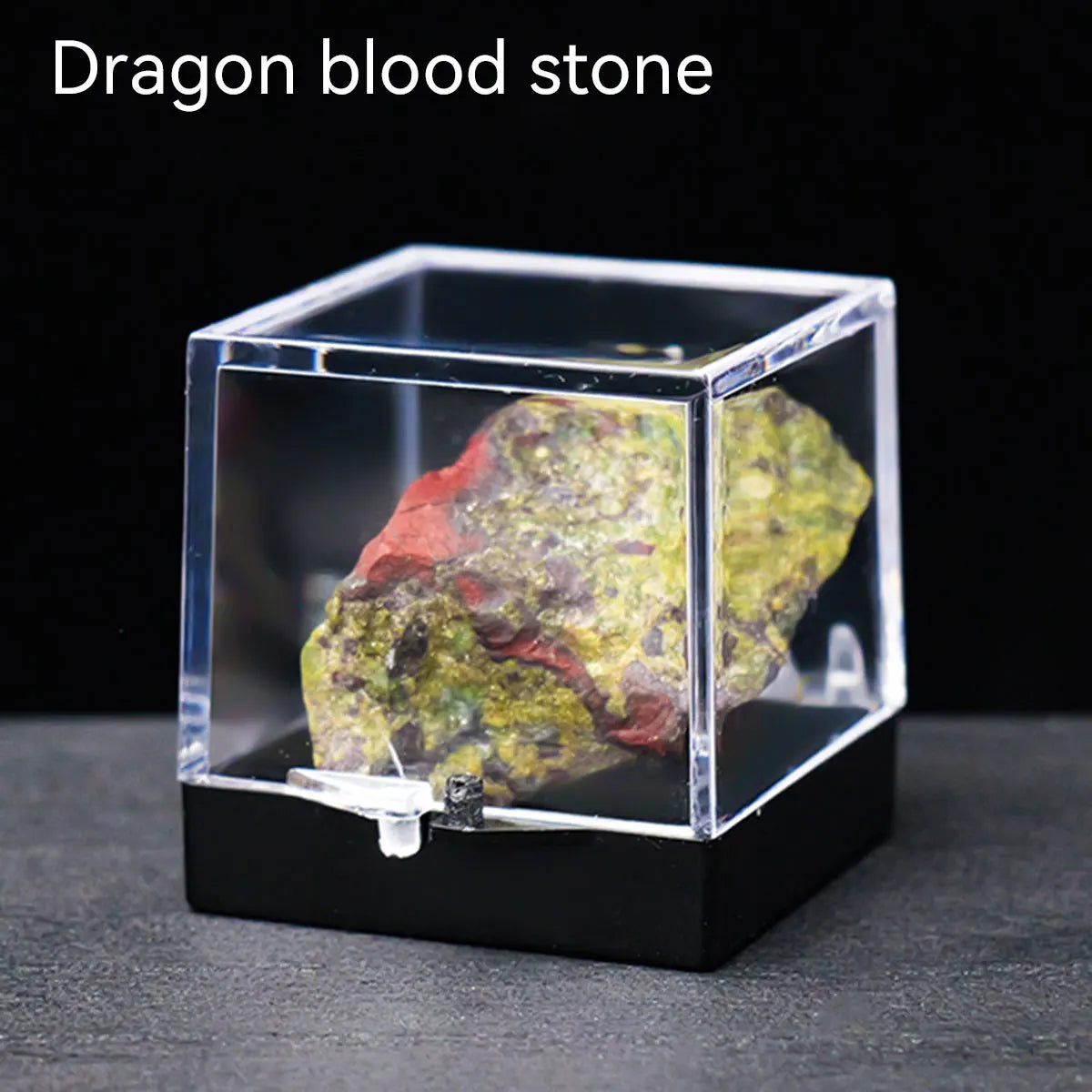A rough, reddish-green dragon blood stone crystal specimen displayed inside a clear glass box.