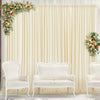 A cream draped backdrop curtain decorated with floral arrangements, featuring white upholstered chairs.