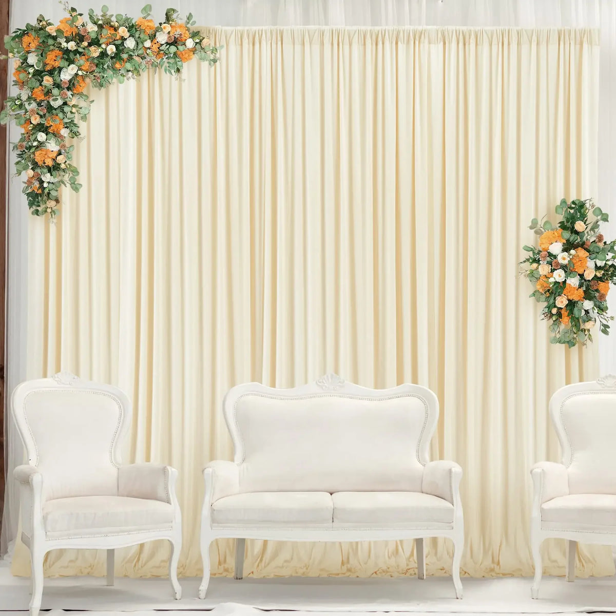 A cream draped backdrop curtain decorated with floral arrangements, featuring white upholstered chairs.