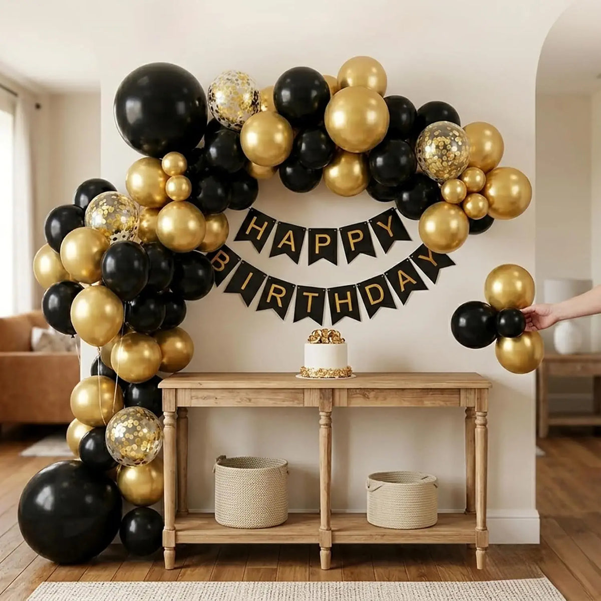 A black and gold balloon garland arch decorated for a birthday, displayed above a wooden shelf.