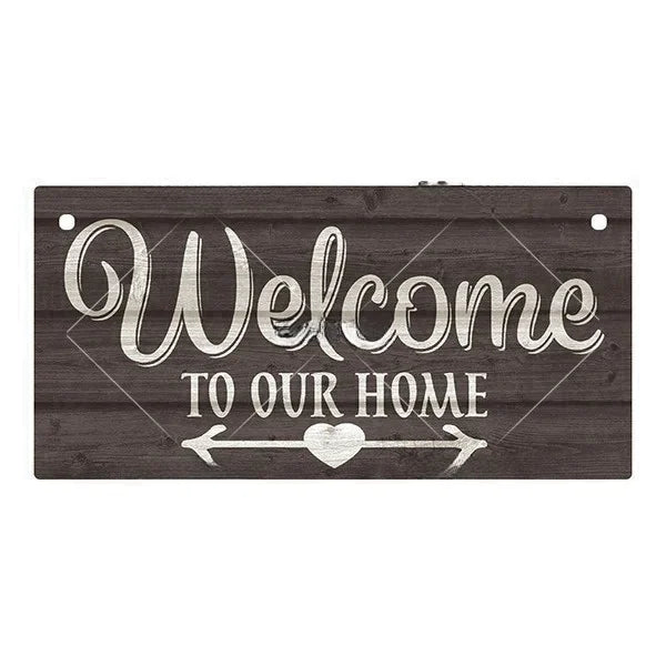 A rustic wooden hanging sign with white script that reads Welcome to our home and features a heart-shaped arrow design.