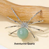 Silver crystal spider figurine with a pale green quartz bead resting on a natural wood surface.