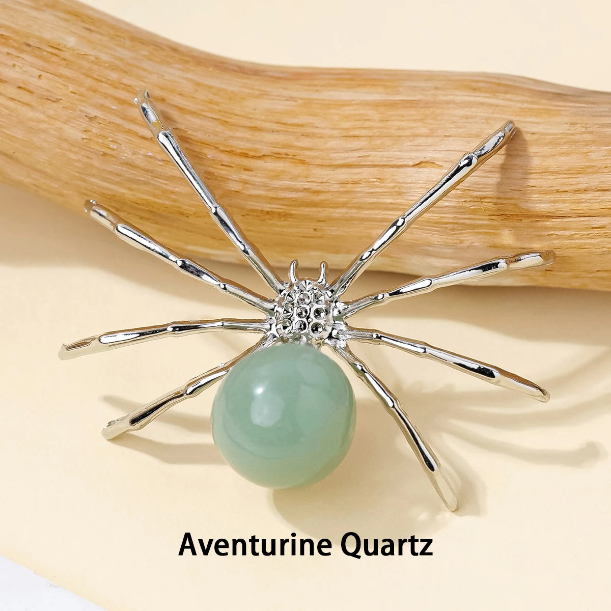 Silver crystal spider figurine with a pale green quartz bead resting on a natural wood surface.
