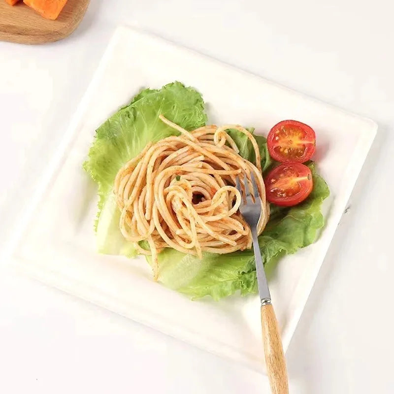 A plate of spaghetti served on a bed of lettuce on a white square paper plate.