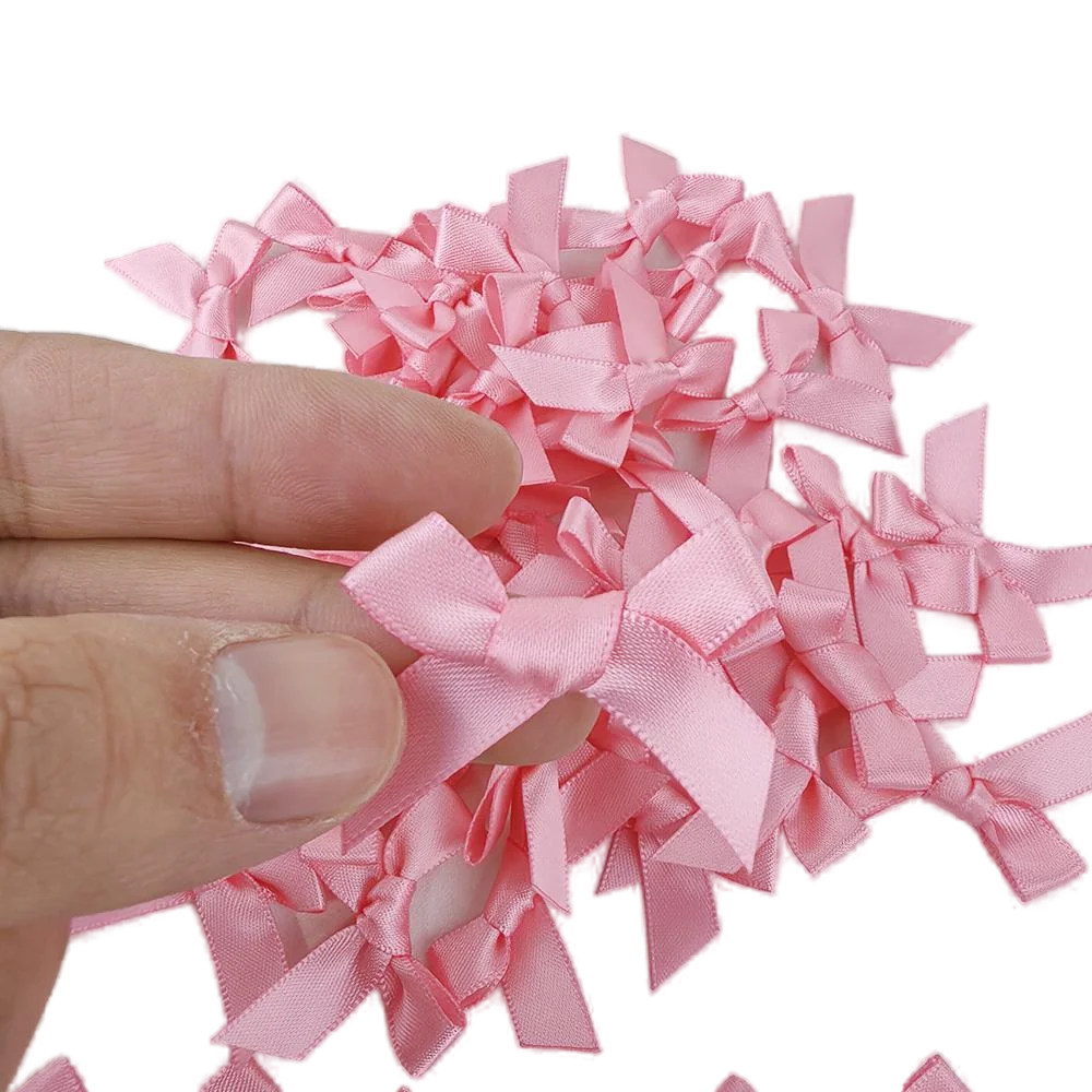 A hand holds a set of pink satin bow cupcake toppers for parties.