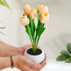 A hand holds a vase of pink tulips in a white ceramic pot, used as an LED night light.