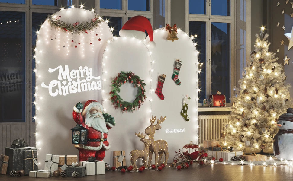 Una exhibición navideña con un arco de fondo elástico blanco decorado con luces, guirnaldas y regalos.