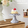 A small gray cupcake stand displaying a single strawberry and cream cupcake on a wooden surface.