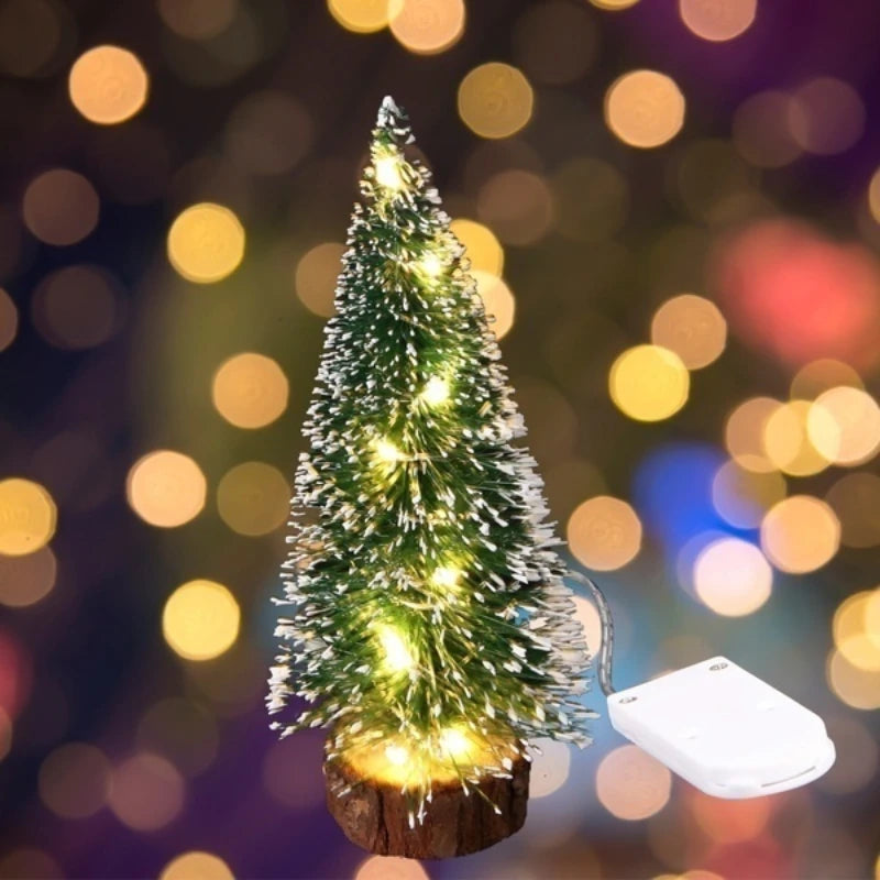 An LED mini Christmas tree with a snow effect is displayed on a wooden base against a blurred bokeh background.