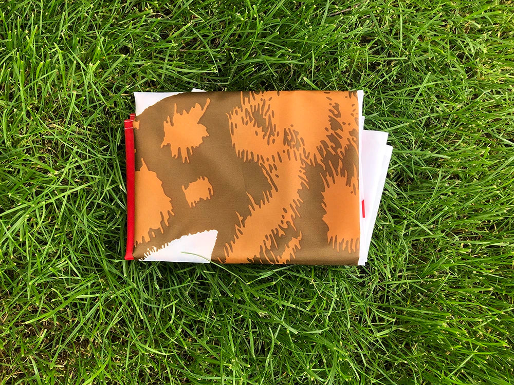 A folded California State Flag in brown and white patterns rests on green grass.