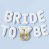 A banner made of white balloon letters spelling BRIDE and TO BE, with a gold diamond ring centerpiece.