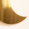 A curved gold acrylic moon wall mirror reflecting light on a white background.