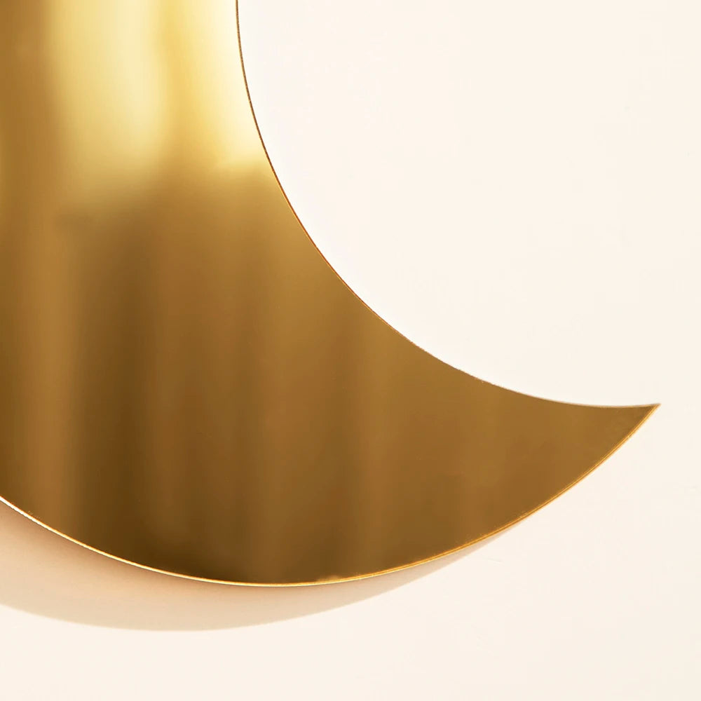 A curved gold acrylic moon wall mirror reflecting light on a white background.