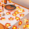 Warm orange maple leaf fairy string lights draped across a white tablecloth.