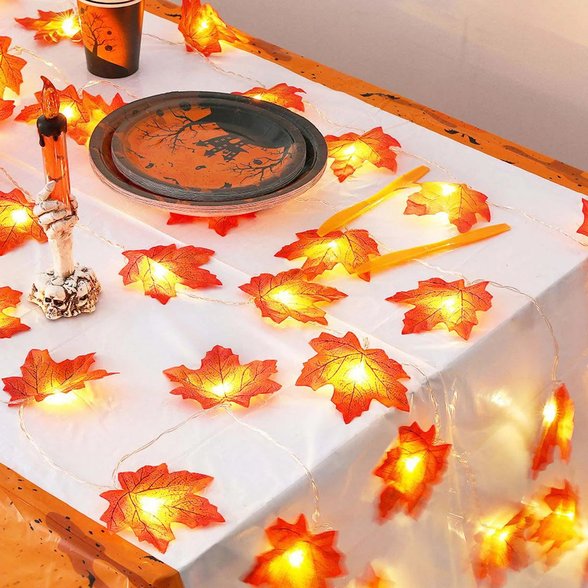 Warm orange maple leaf fairy string lights draped across a white tablecloth.
