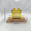 A golden statue of the Ark of the Covenant with wings, displayed on a brown wooden base.