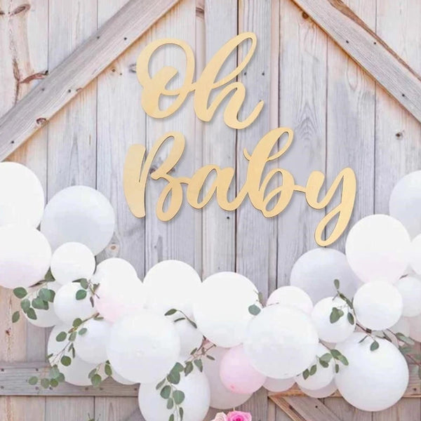 Gold wooden sign spelling out Oh Baby decorated with white balloons and greenery