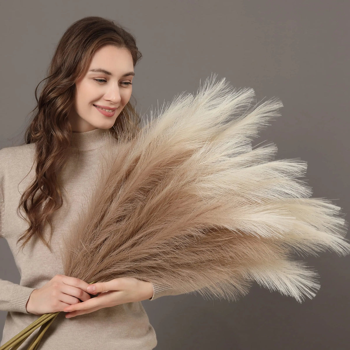A woman holds a large bundle of beige artificial pampas grass branches for decor.