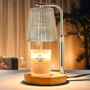 A modern silver adjustable electric candle warmer lamp with a clear glass shade illuminating a scented candle on a wooden bas