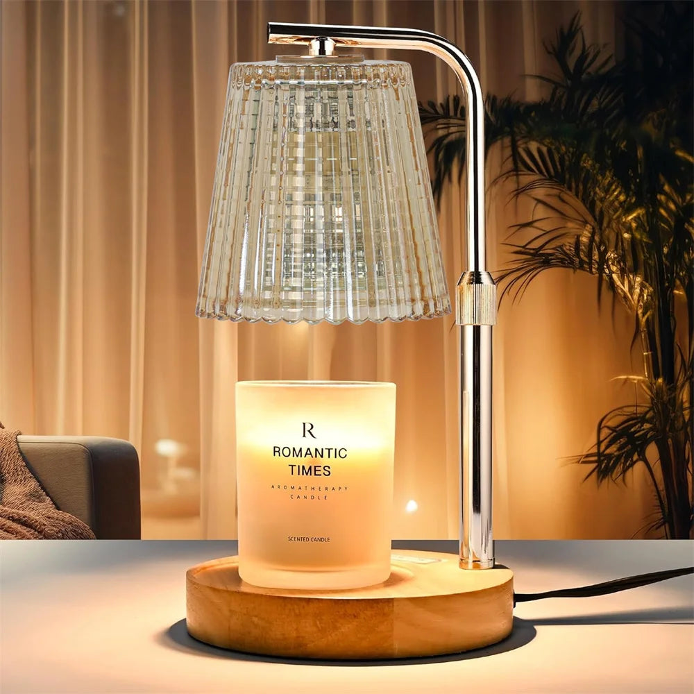 A modern silver adjustable electric candle warmer lamp with a clear glass shade illuminating a scented candle on a wooden bas