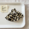 A leopard print shoulder strap skirt for dolls is displayed on a white plate next to a handwritten note.