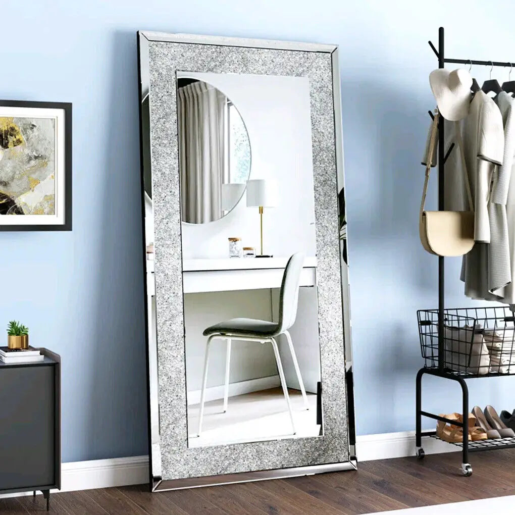 A rectangular silver crystal rhinestone wall mirror with a sparkling frame hanging on a light blue wall.